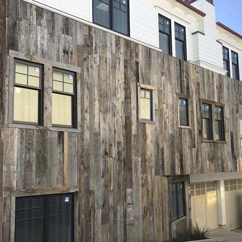 Grey reclaimed wood siding hung vertically as cladding on a modern apartment complex.