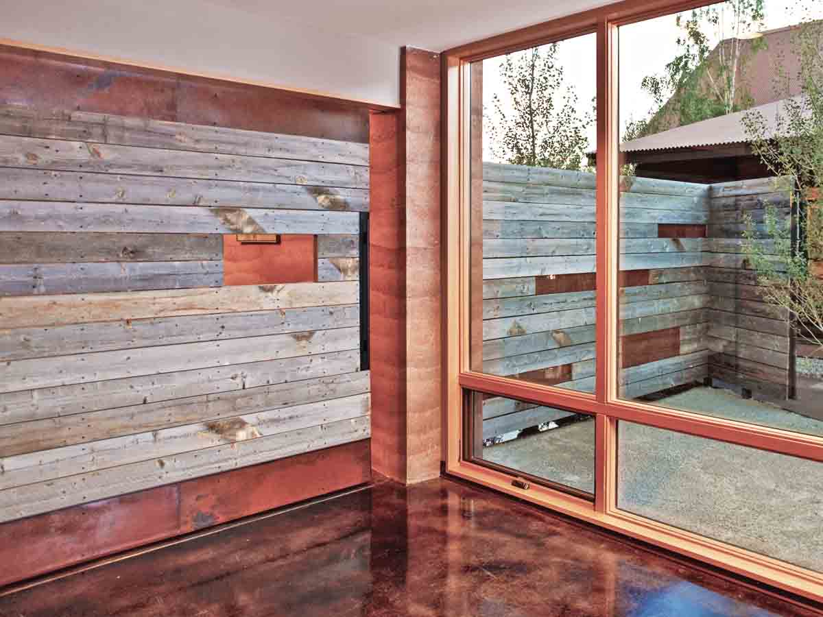 Aged metal and reclaimed wood interior and exterior walls separated by a window in a public library.