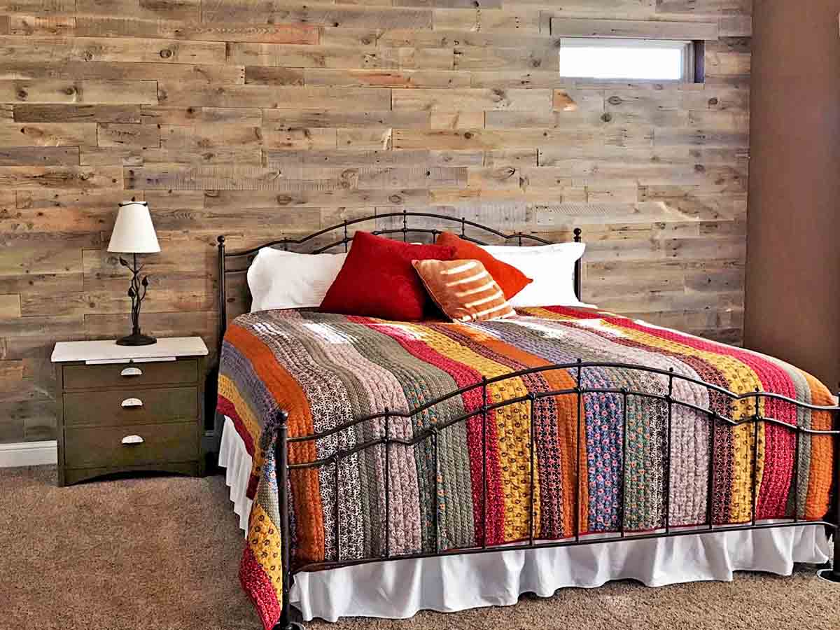 Reclaimed wood accent wall in a traditional bedroom with a colorful quilted bedspread.