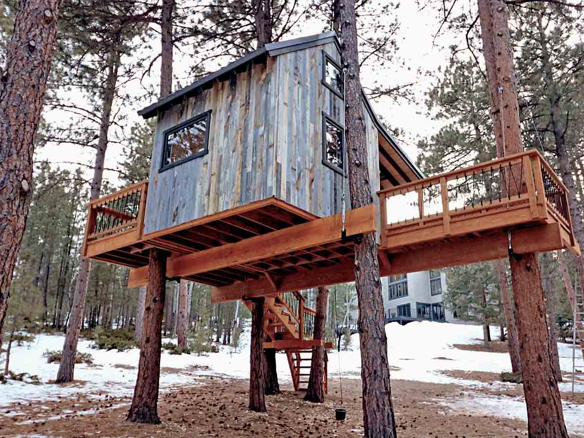 Tree house with vertical, grey reclaimed wood siding in the winter.