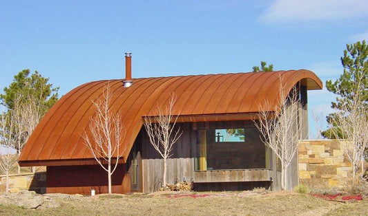 A modern house with reclaimed wood siding and an arched aged metal roof.