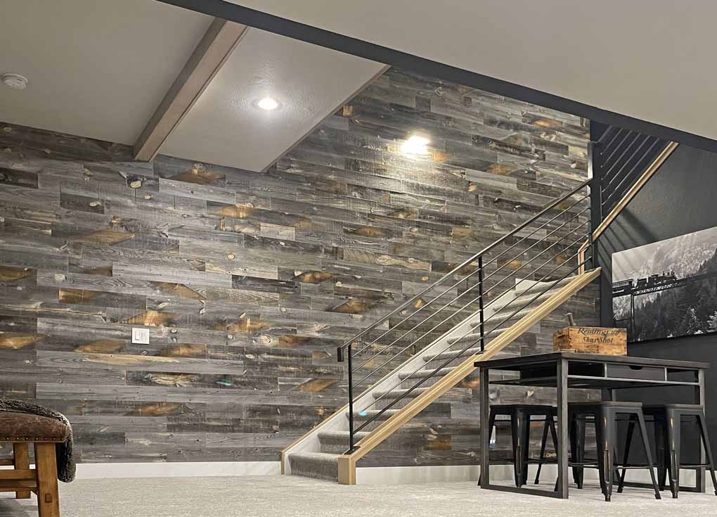 Basement renovation with a grey reclaimed wood wall and black accent furniture and paint.