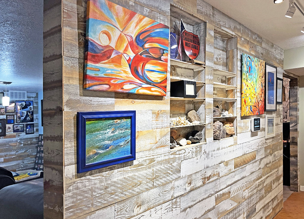 Distressed white reclaimed wood wall with recessed shelves and colorful paintings hung on the wall