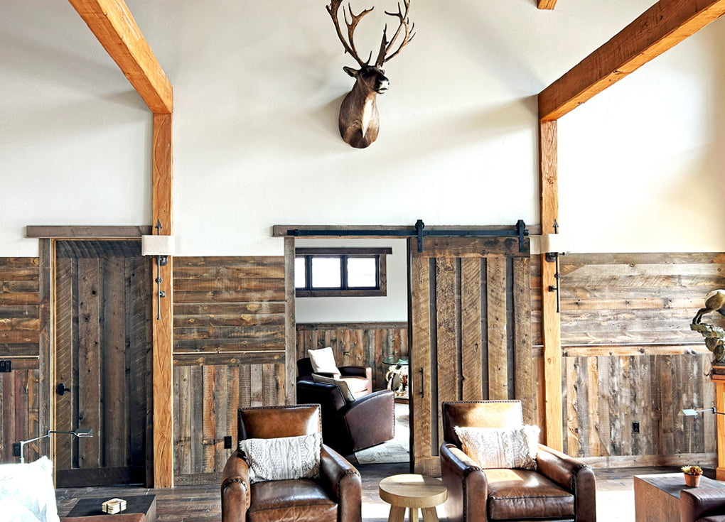 Brown, Saratoga reclaimed wood planks on the wall of a mountain lodge with  leather arm chairs and a  mounted deer head.