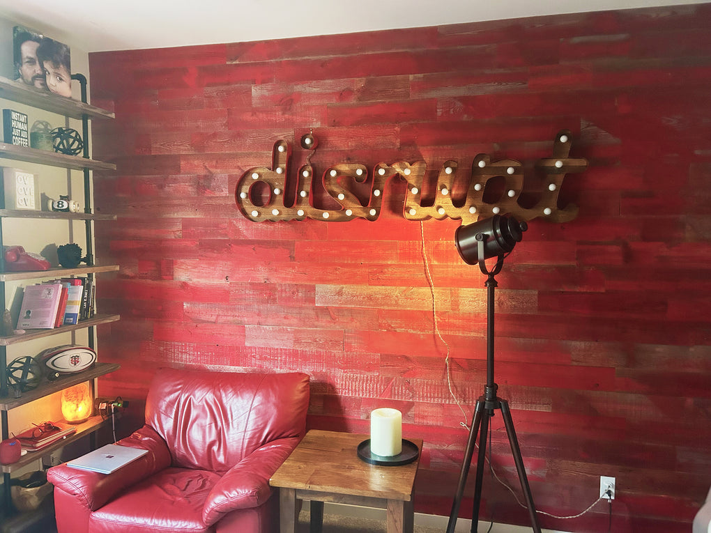 Red barn wood wall in a boho style living room with a lighted sign that reads DISRUPT.