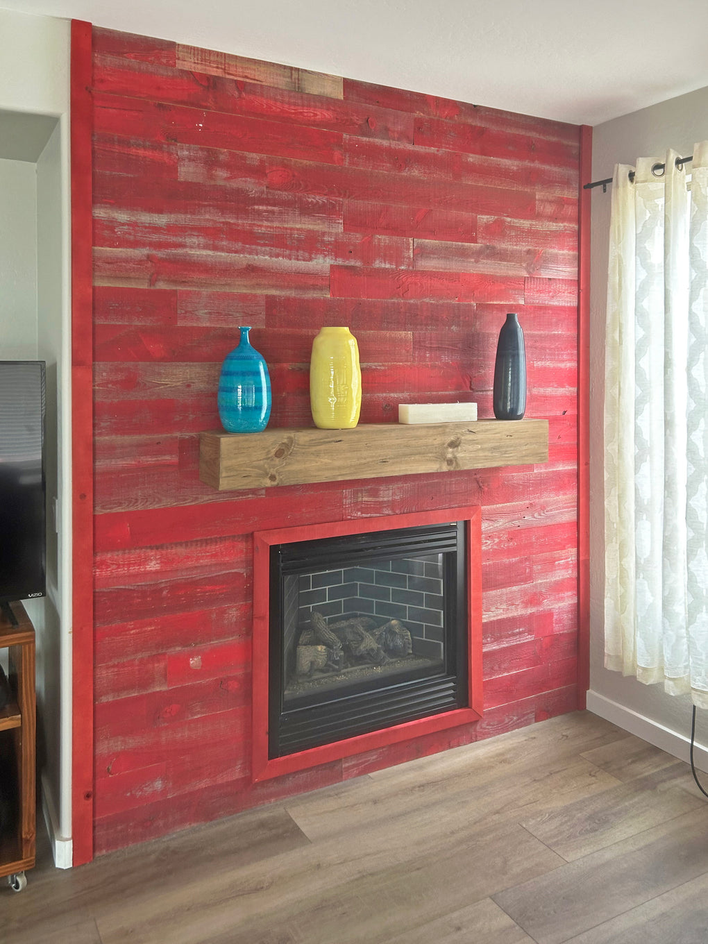 Painted red barn wood fireplace surround with 3 colorful vases on a mantel.