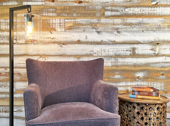 Distressed whitewash wood paneling on a wall in a den with a purple chair and farmhouse style lamp.