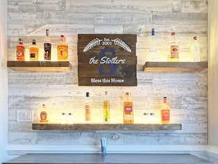 Custom home bar with a whitewashed reclaimed wood background and three floating shelves for bottles.