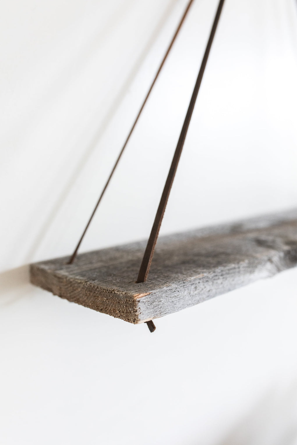 Close up image of a reclaimed wood shelf with thin, brown leather straps
