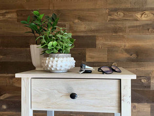 Wooden plank wall in the brown Saratoga finish on a bedroom wall with awhite nightstand with plants, car keys, and glasses.